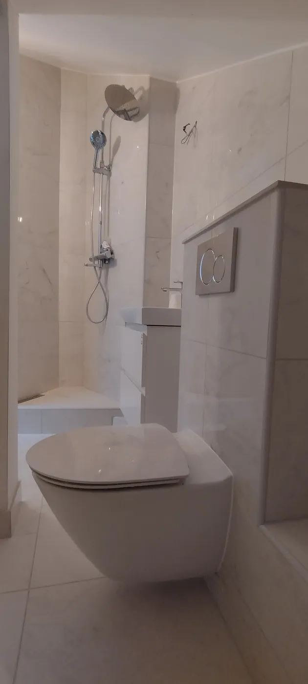 Badrum i marmormönstrad kakel med vägghängd wc och inbyggt badkar