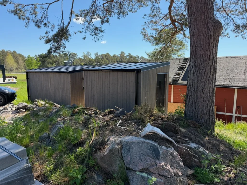 Träklädd komplementbyggnad med plåttak, uppförd på bergig tomt