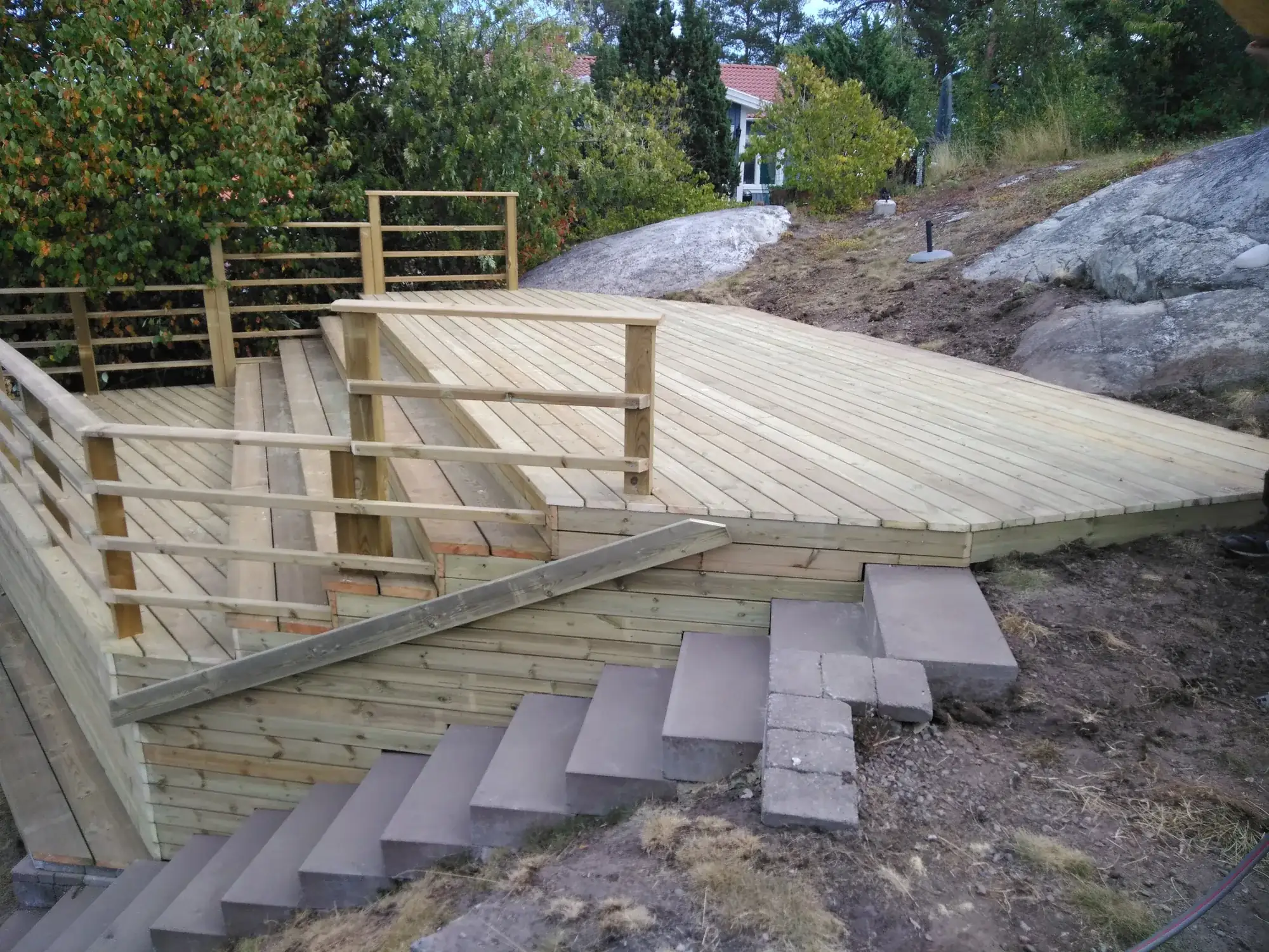 Trädäck med räcke på en klipptomt, med trappa i betongsteg ner mot marken