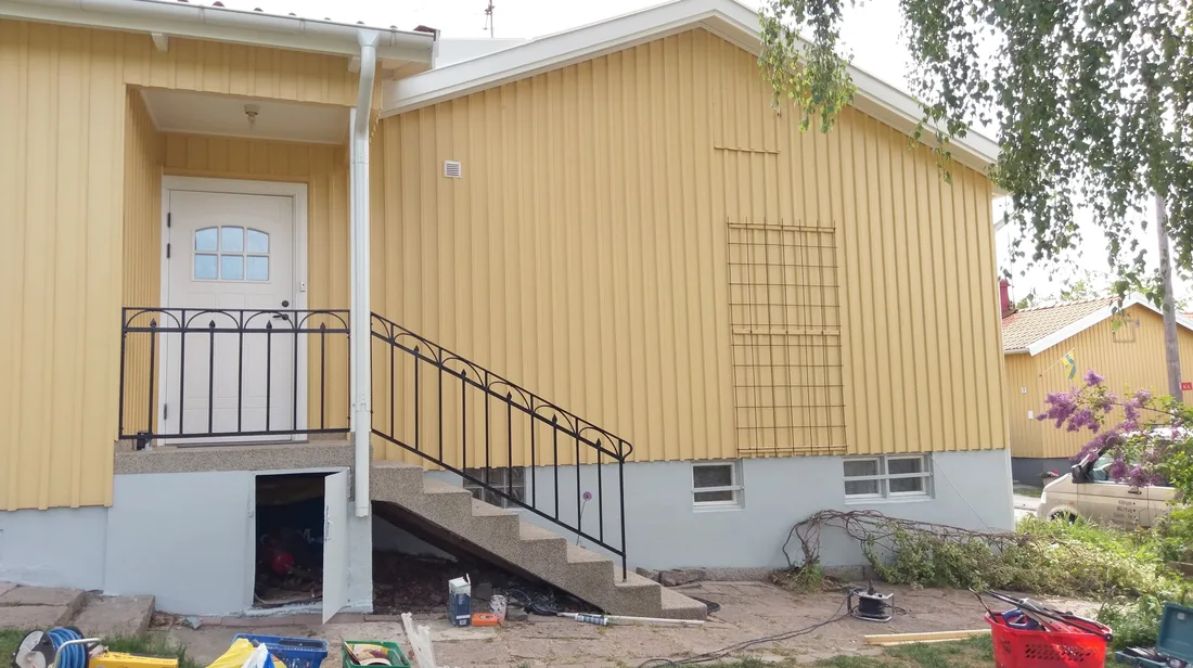 Färdigmålad gul träfasad med vit entré, smidesräcke och nymålad sockel